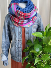 Load image into Gallery viewer, A blue chunky-knit infinity scarf styled around a mannequin torso wearing a denim jacket and rust-colored top, with a green plant in the foreground.