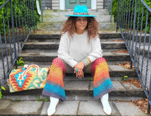 Load image into Gallery viewer, Black woman wearing a turquoise hat with a white sweater, a Southwestern bag and crochet pants in grey, green, red, orange, gold and turquoise.