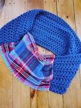Load image into Gallery viewer, A blue crocheted cowl neck warmer with a matching blue and pink plaid fabric lining, displayed with a wood background. 
