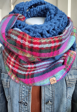 Load image into Gallery viewer, A chunky knit infinity scarf in a vibrant multicolor plaid pattern with a thick blue textured knit inner layer, displayed on a mannequin wearing a denim jacket.

